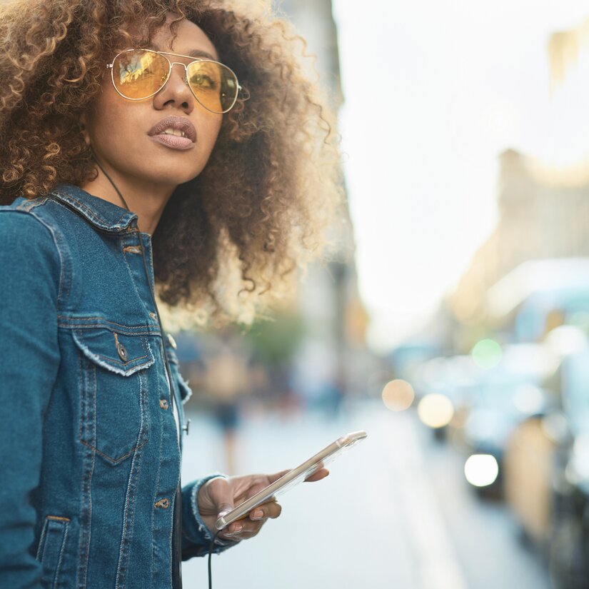 Pige med solbriller og smartphone, der kigger efter en KINTO Share delebil